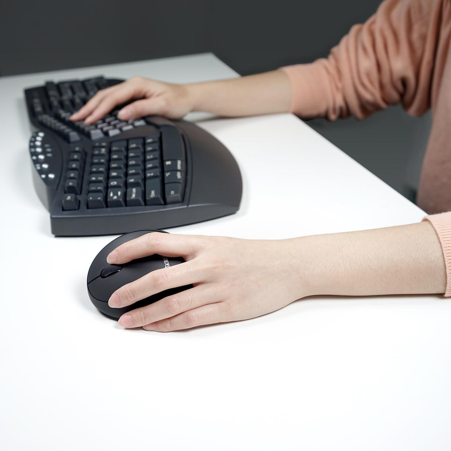 Eine Person tippt auf einer geteilten Tastatur und benutzt eine Maus.