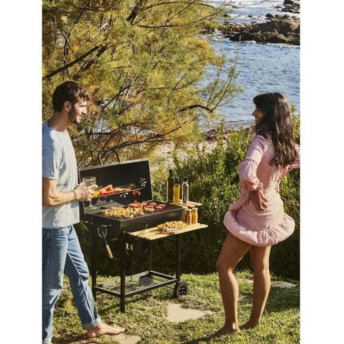 Man en vrouw barbecueën aan zee. Eten op de grill, oceaan op achtergrond.