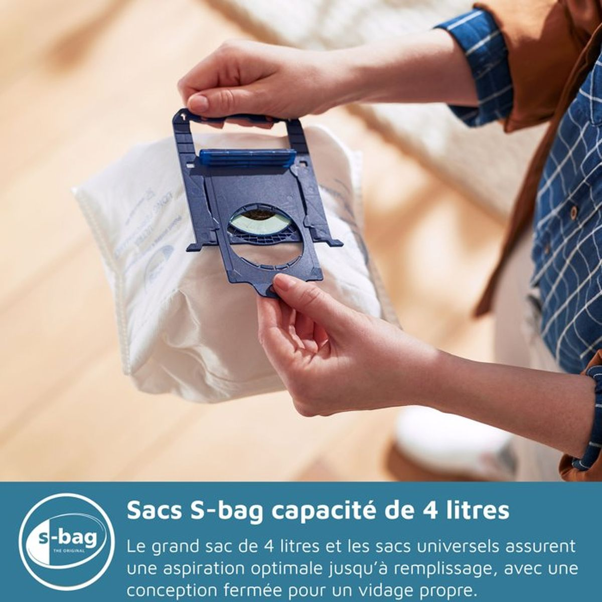 Osoba trzyma niebieski uchwyt worka do odkurzacza na białym worku do odkurzacza.