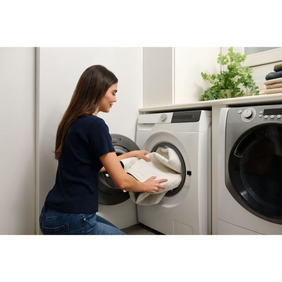 Kobieta klęczy przed pralką, wkładając pranie.