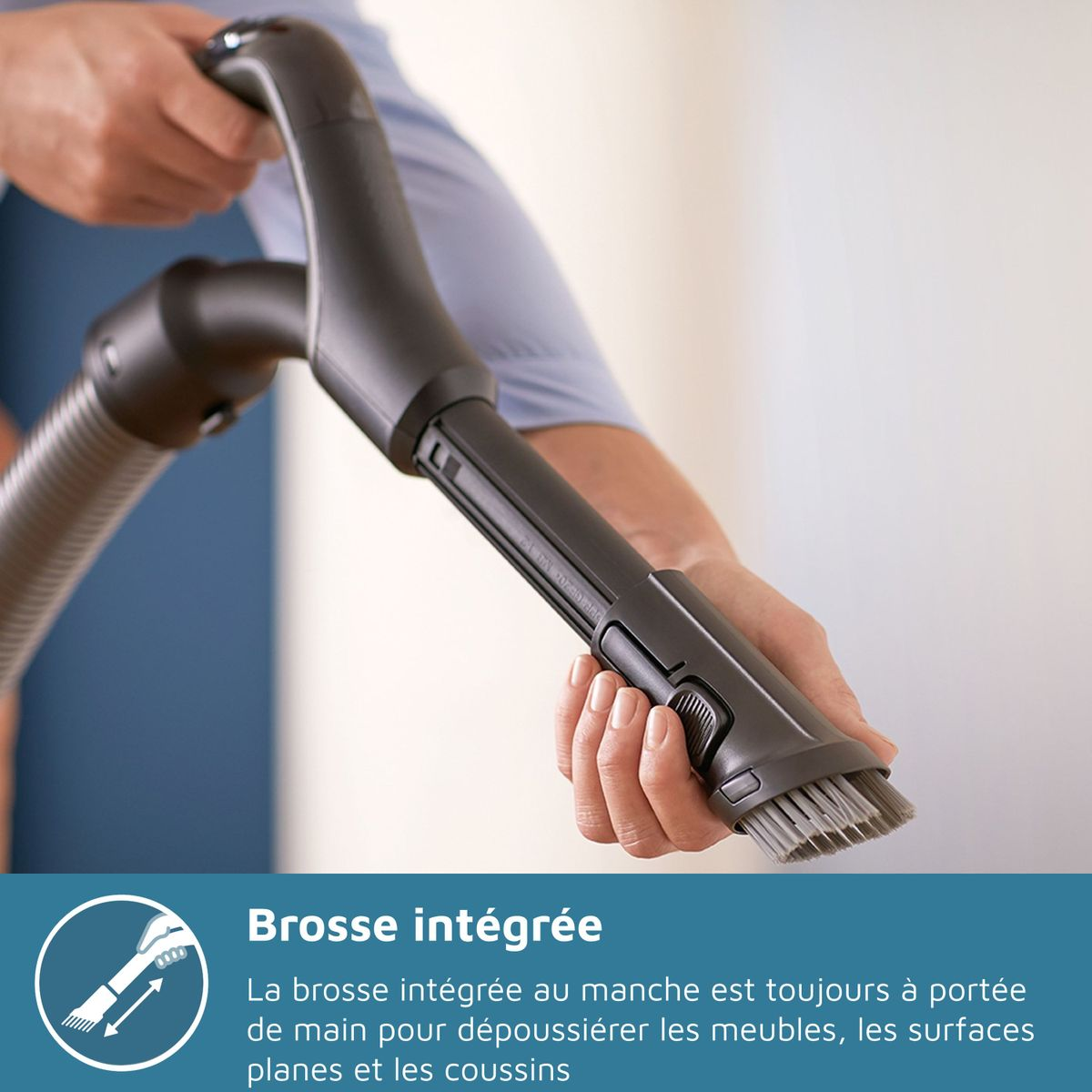 Ręka trzyma uchwyt odkurzacza ze zintegrowaną szczotką.