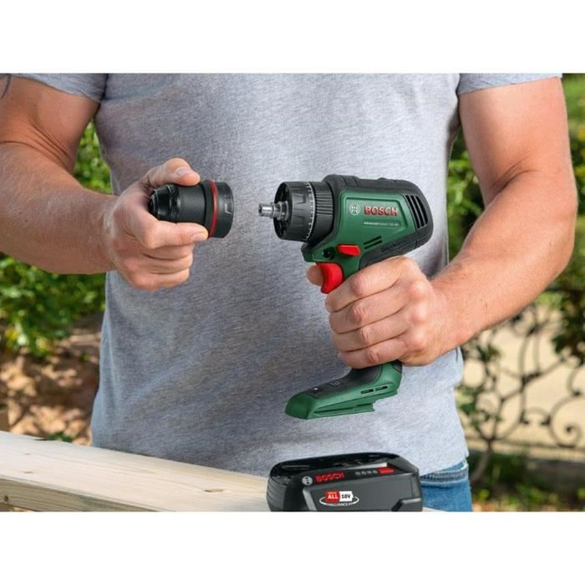 Mann wechselt Bohrfutter an grüner Bosch Bohrmaschine neben Holz.