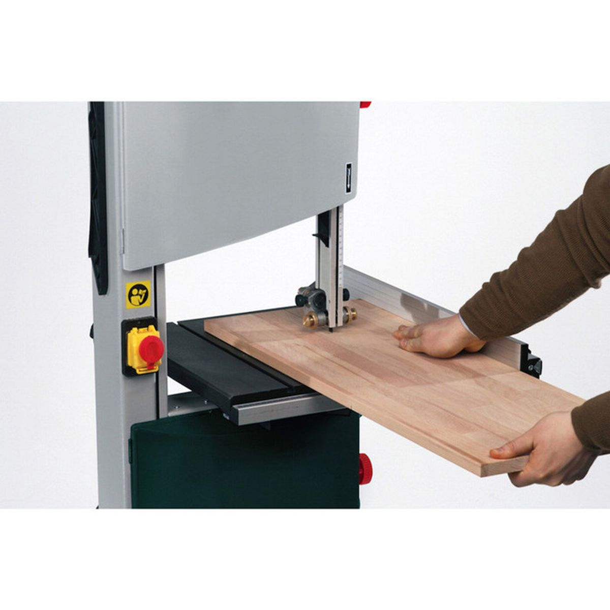 Une personne coupe une planche de bois sur une scie à ruban. Mains guident le bois.