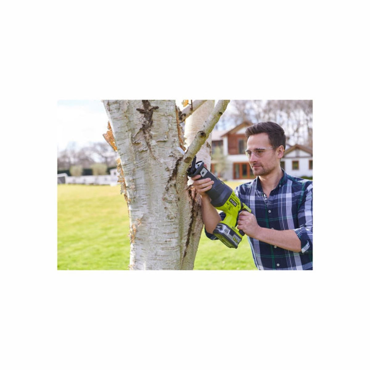 Hombre cortando rama de árbol en jardín con sierra.