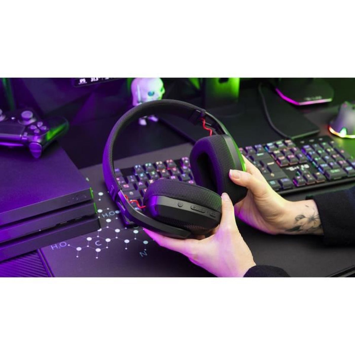 Hände halten schwarze Kopfhörer über Tastatur und Konsole mit Lila-Licht.