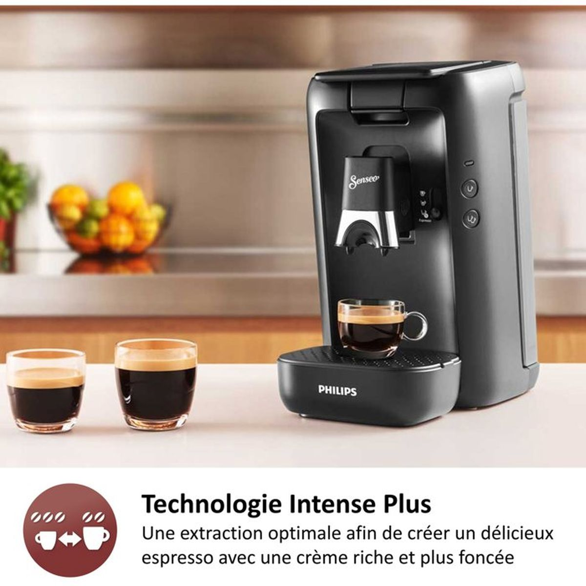 Eine schwarze Kaffeemaschine mit zwei Espressotassen und Obst im Hintergrund.