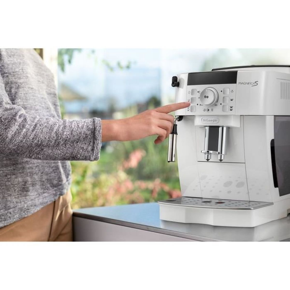 Una mano preme un pulsante su una macchina da caffè bianca con accenti argentati.