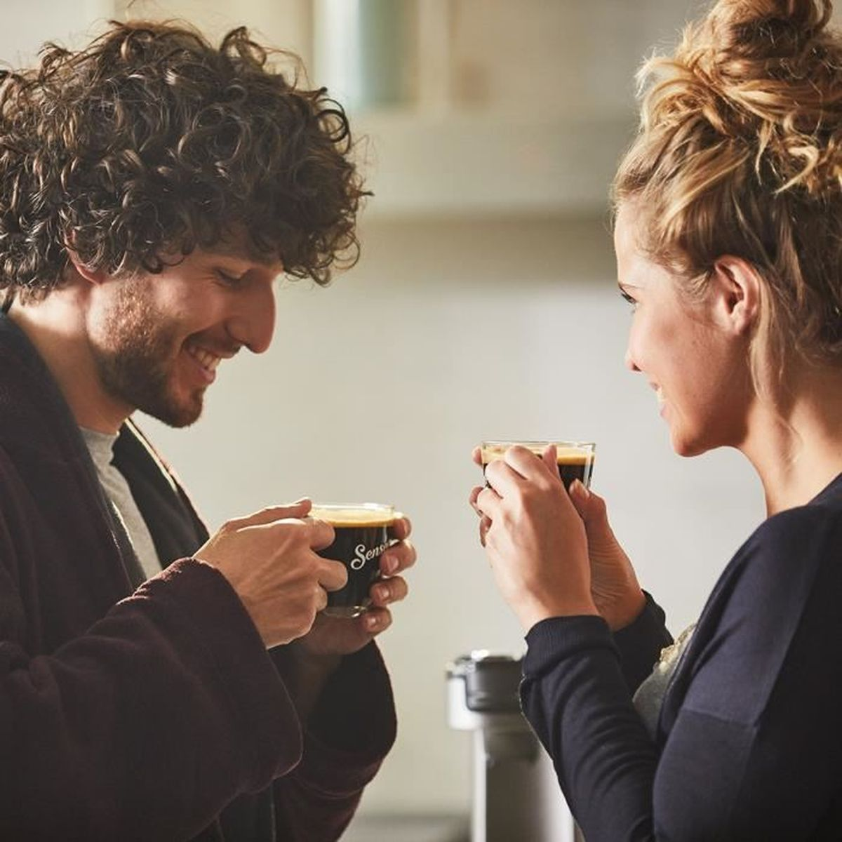 Mężczyzna i kobieta uśmiechają się do siebie z filiżankami kawy.