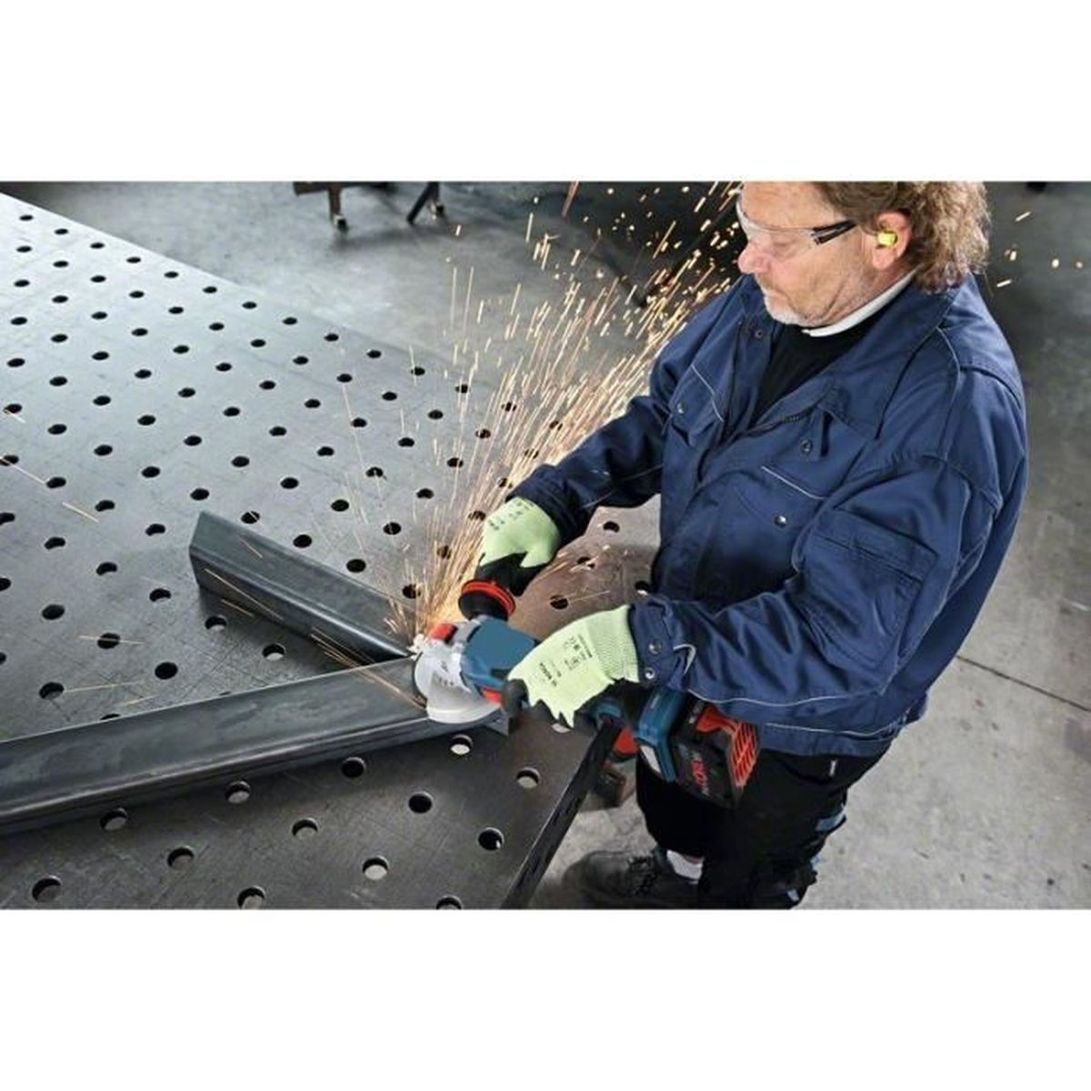 Mężczyzna szlifuje metal szlifierką kątową, lecą iskry.