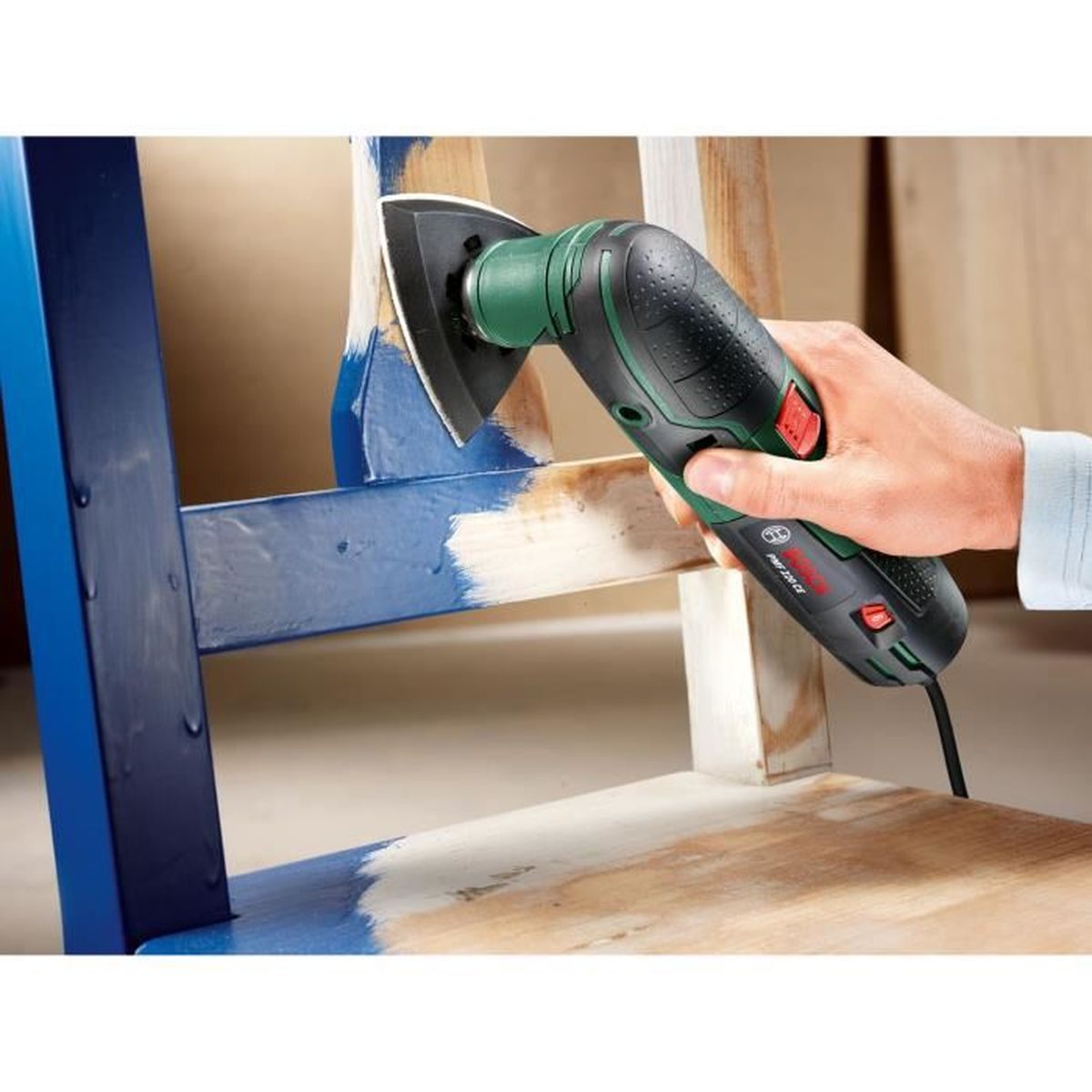 Ein Mann schleift blaue Farbe von einem Holzstuhl ab.