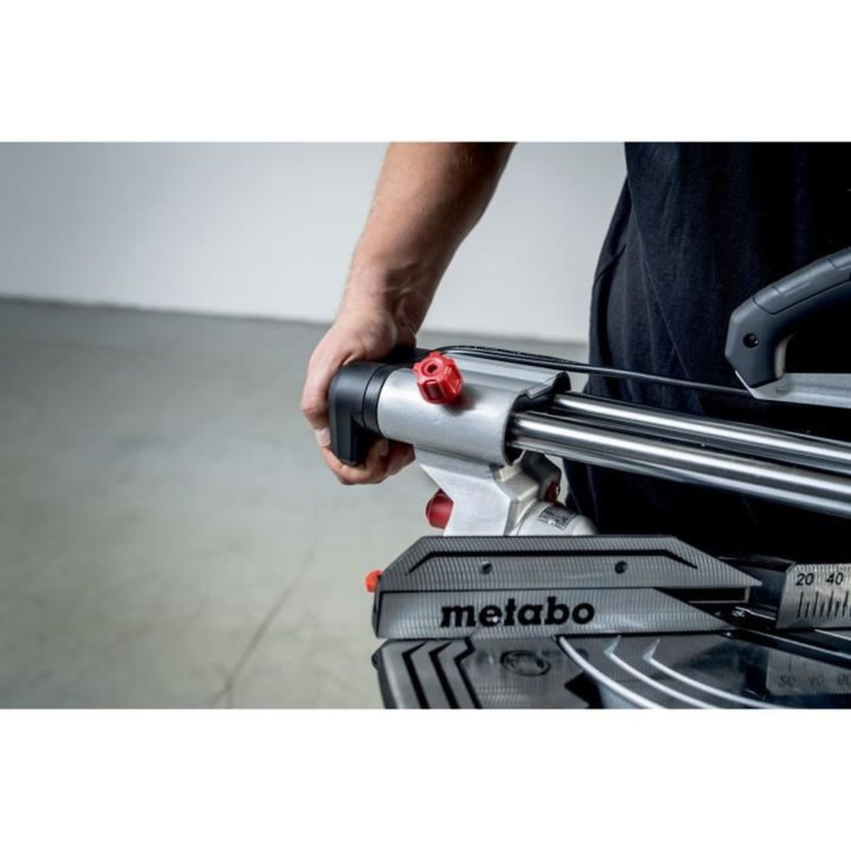 Een hand pakt een rode knop vast op een Metabo-zaag met metalen rails.