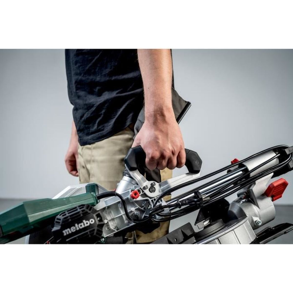 Man met een Metabo-afkortzaag, grijze achtergrond.