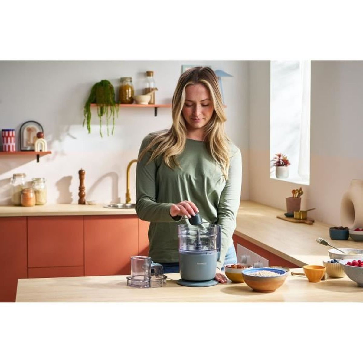 Una donna con top verde usa un robot da cucina in cucina.