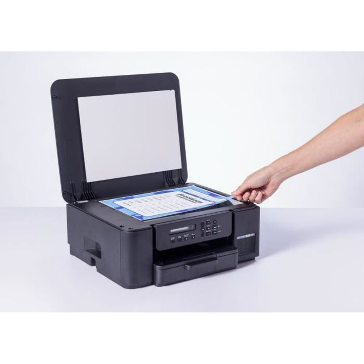 Ręka wkłada papier do otwartej drukarki.