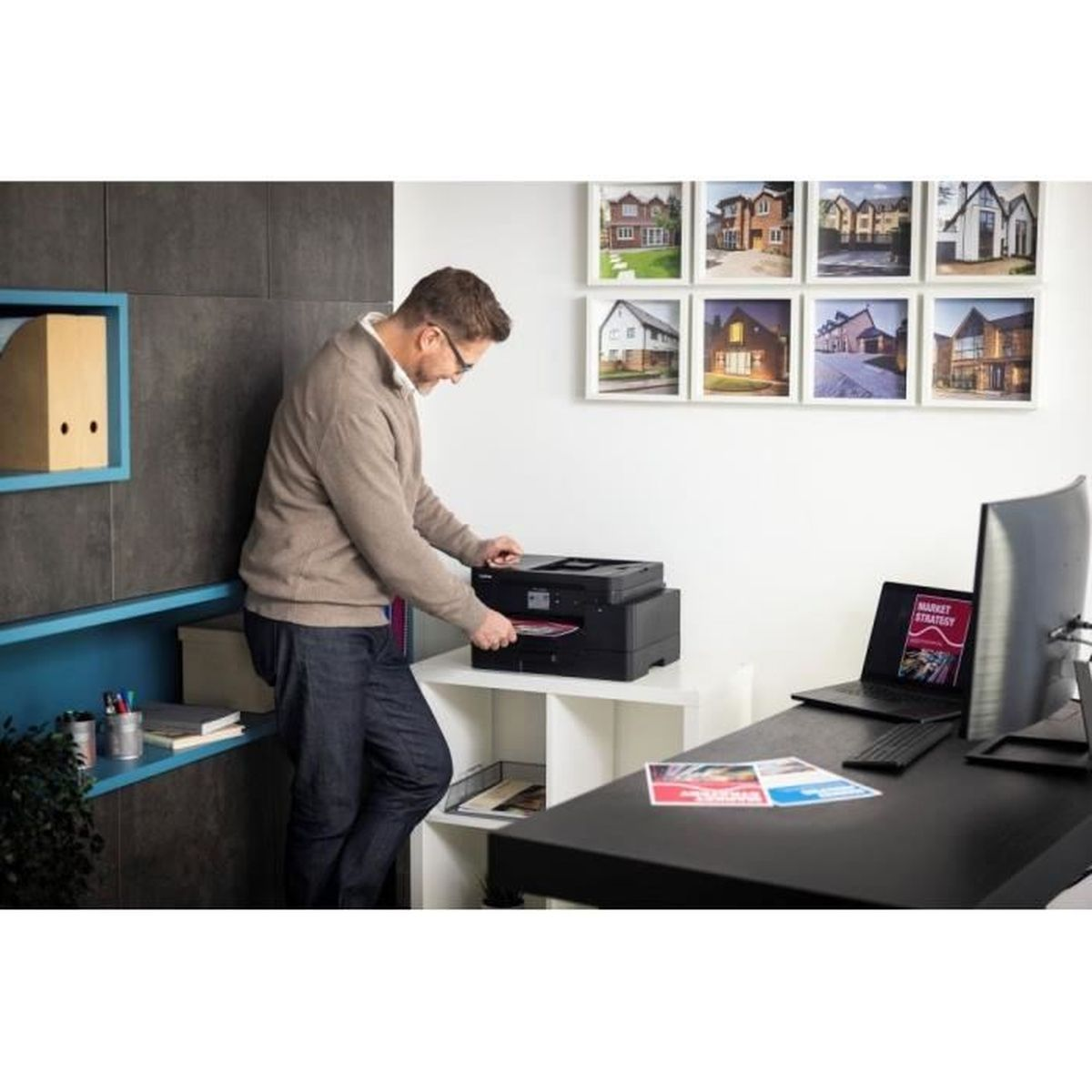 Een man gebruikt een printer in een kantoor met foto's van huizen aan de muur.