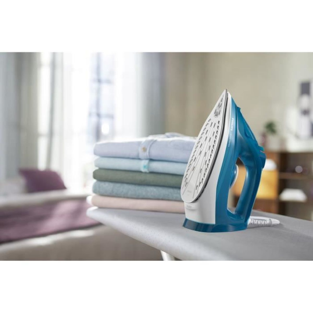 Niebiesko-białe żelazko stoi na desce do prasowania obok stosu ubrań.