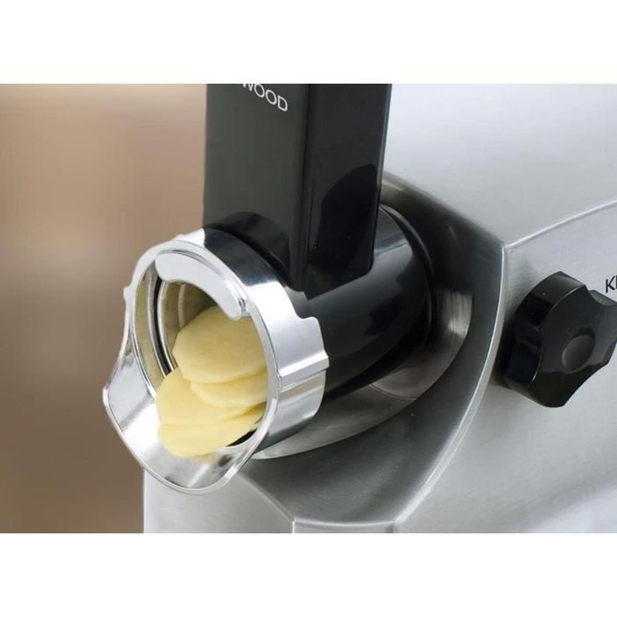 Zbliżenie na maszynkę do mielenia mięsa z żółtymi plasterkami wpadającymi przez srebrny otwór.