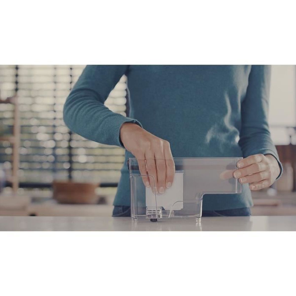 Eine Person setzt einen weißen Filter in einen transparenten Wassertank ein.