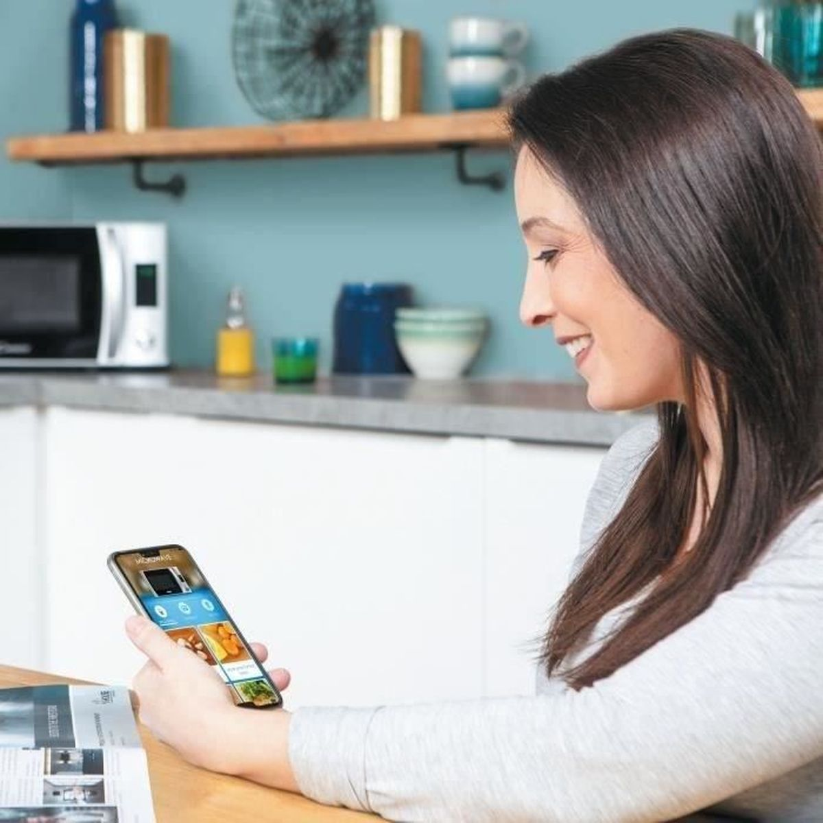 Una donna guarda il suo smartphone in una cucina con microonde.