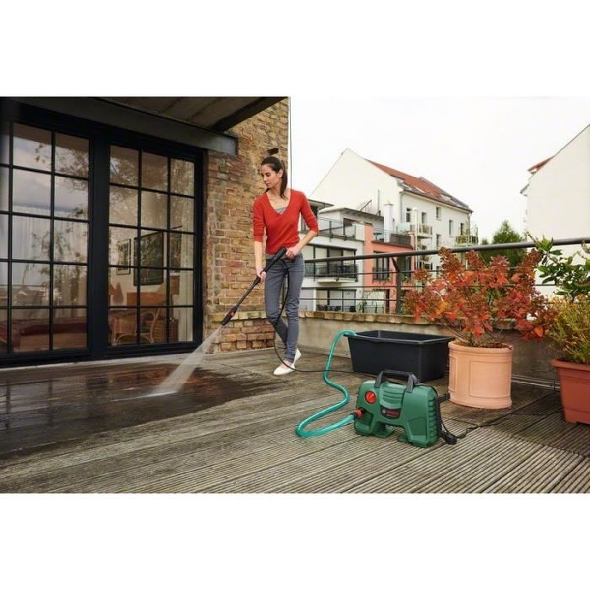 Vrouw reinigt balkon met hogedrukreiniger. Groene machine, zwarte bak, planten.