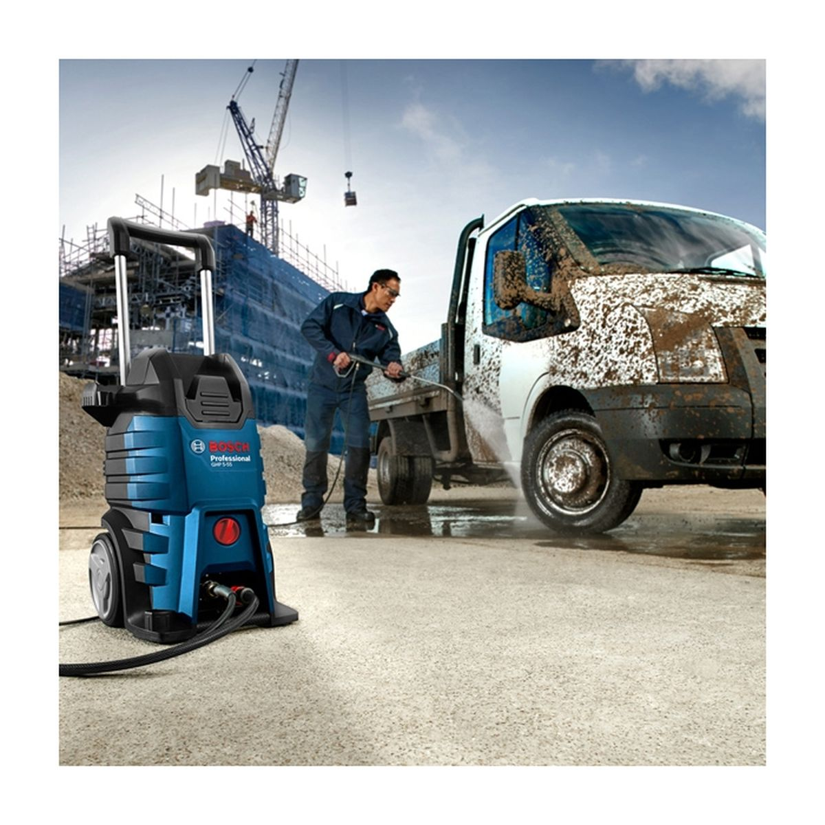 Uomo pulisce camion fangoso con idropulitrice vicino cantiere.
