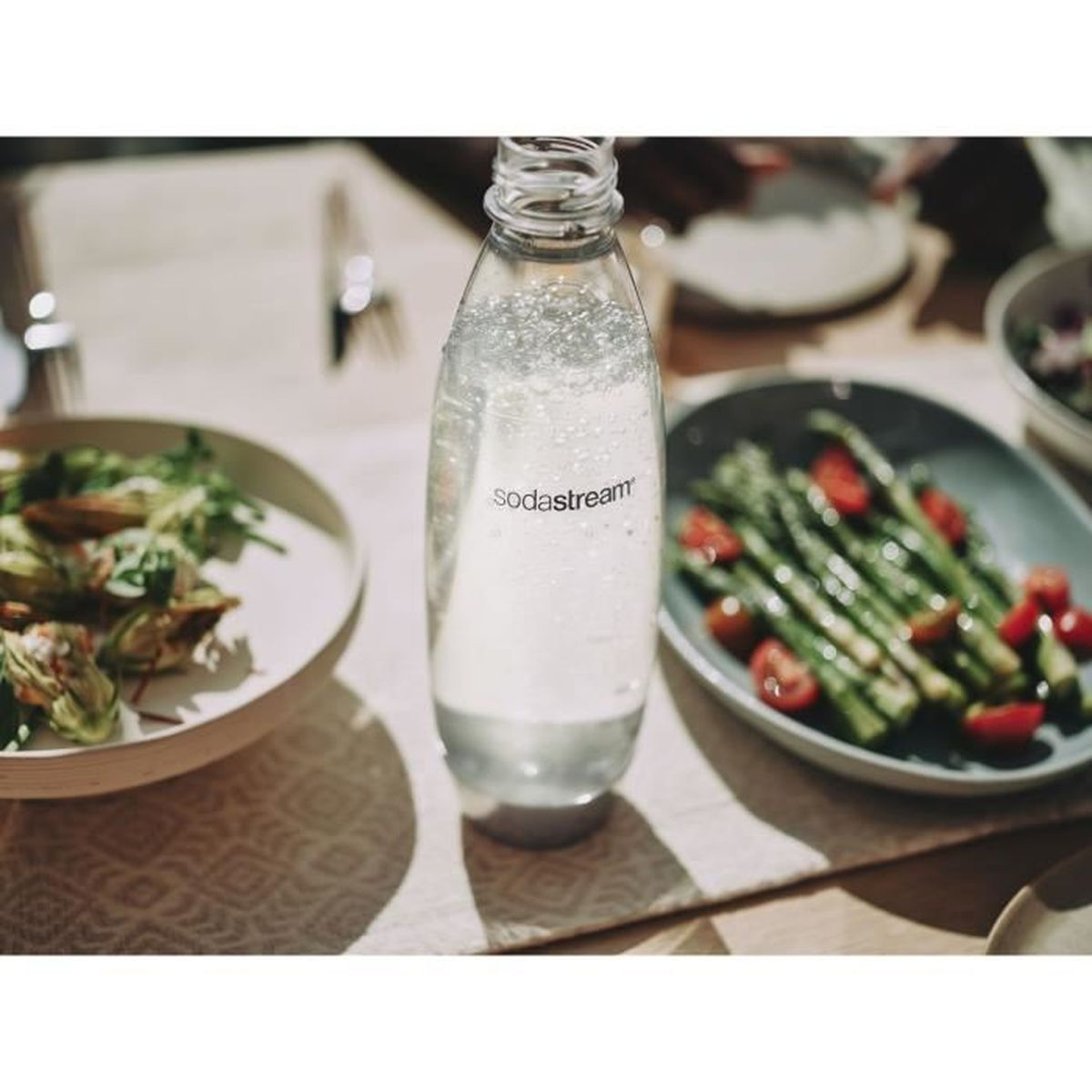 Una bottiglia Sodastream su un tavolo accanto a insalate e asparagi.