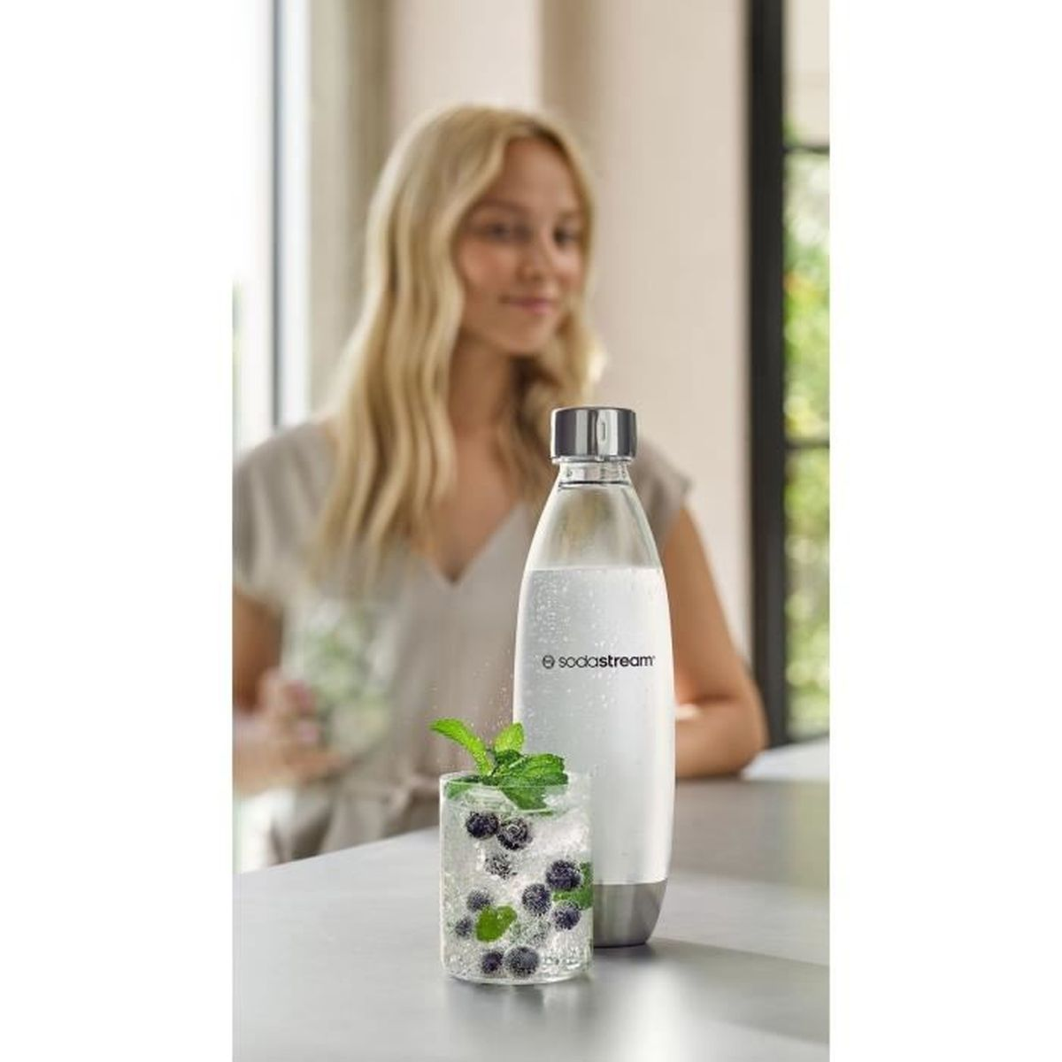 Donna con bottiglia Sodastream e bicchiere con mirtilli e menta.