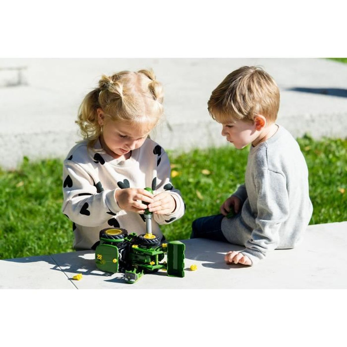 Due bambini assemblano un trattore giocattolo verde all'aperto.