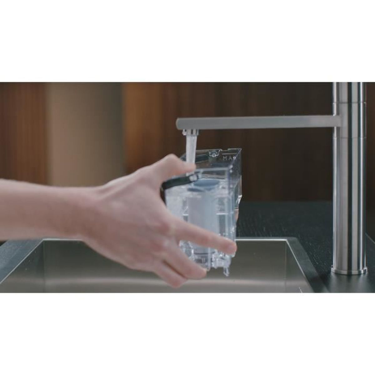 Mano riempie un serbatoio dell'acqua trasparente sotto un rubinetto sopra un lavandino.