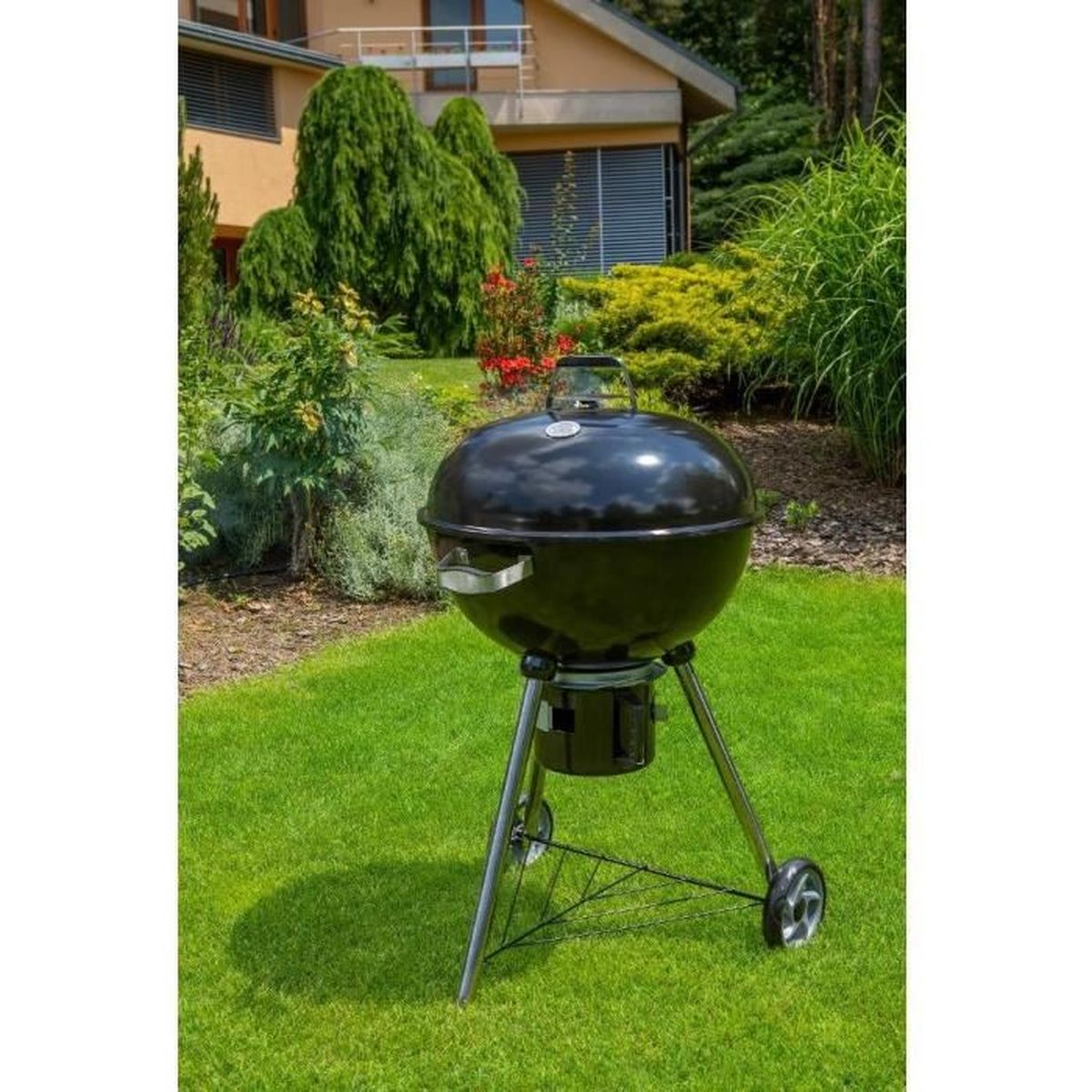 A black grill stands on green grass in front of a house and trees.