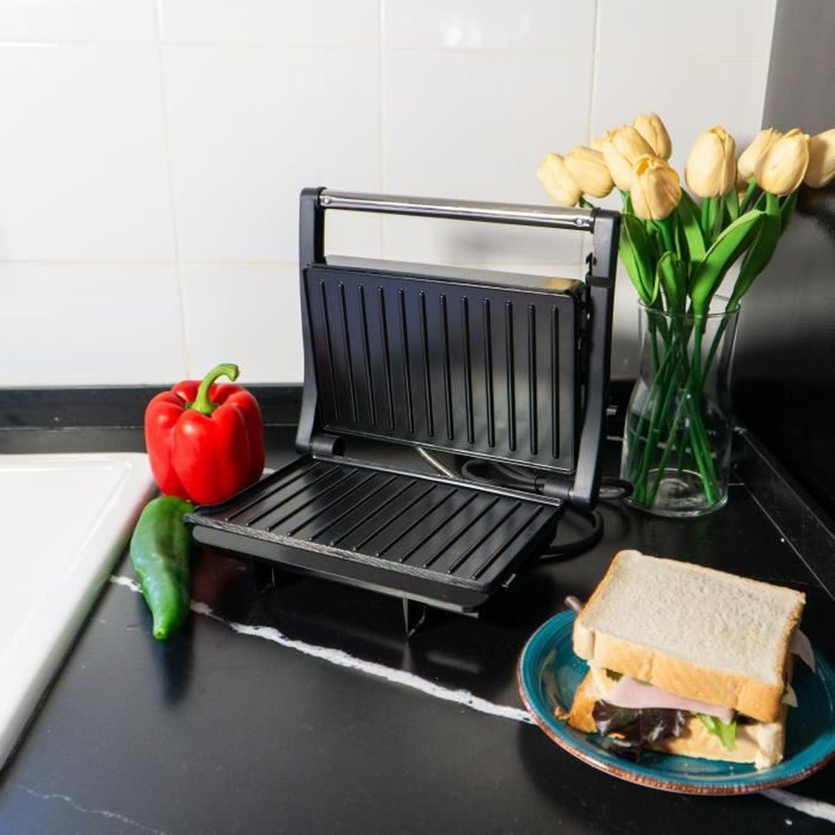 Sandwichera con un sándwich, pimientos y tulipanes.