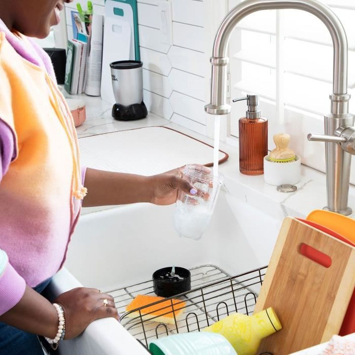 Una persona sciacqua un bicchiere sotto acqua corrente in un lavandino. Diverse taglieri sono vicini.