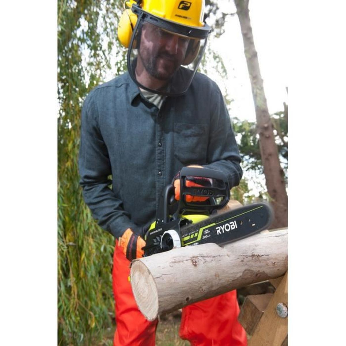 Mężczyzna w kasku z piłą łańcuchową na pniu na zewnątrz.