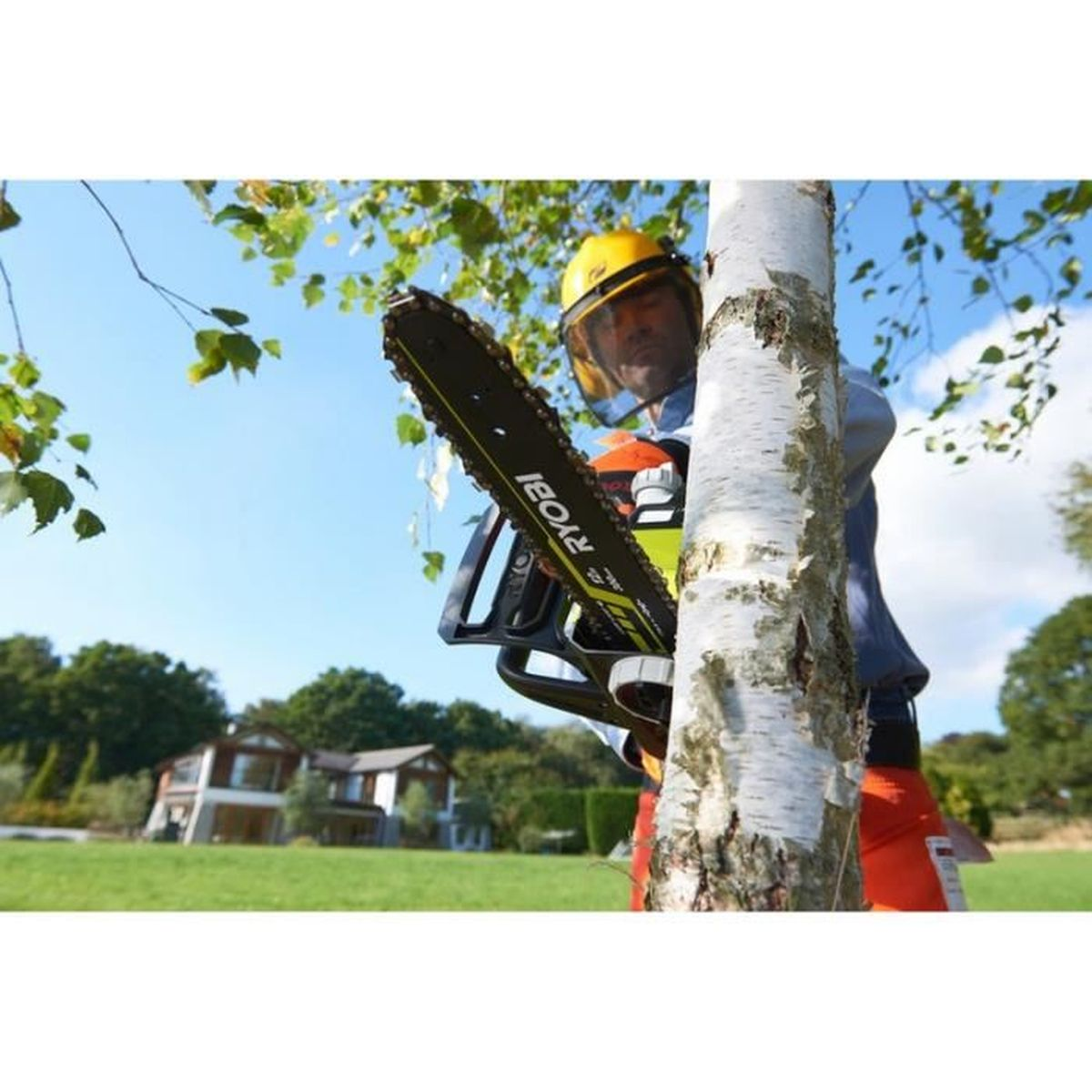 Mężczyzna w kasku z piłą łańcuchową tnie drzewo. Dom w tle.