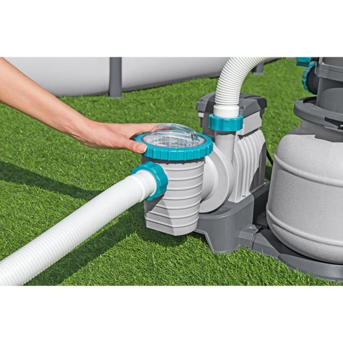 Ręka dotyka pokrywy filtra basenowego obok pompy.