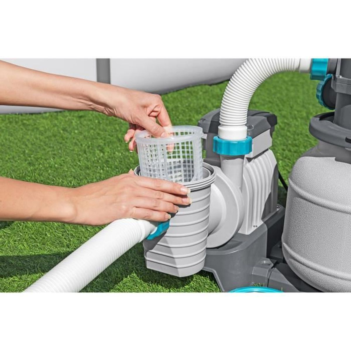 Ręce wkładają biały koszyk filtra do szarej pompy basenowej na zielonej trawie.