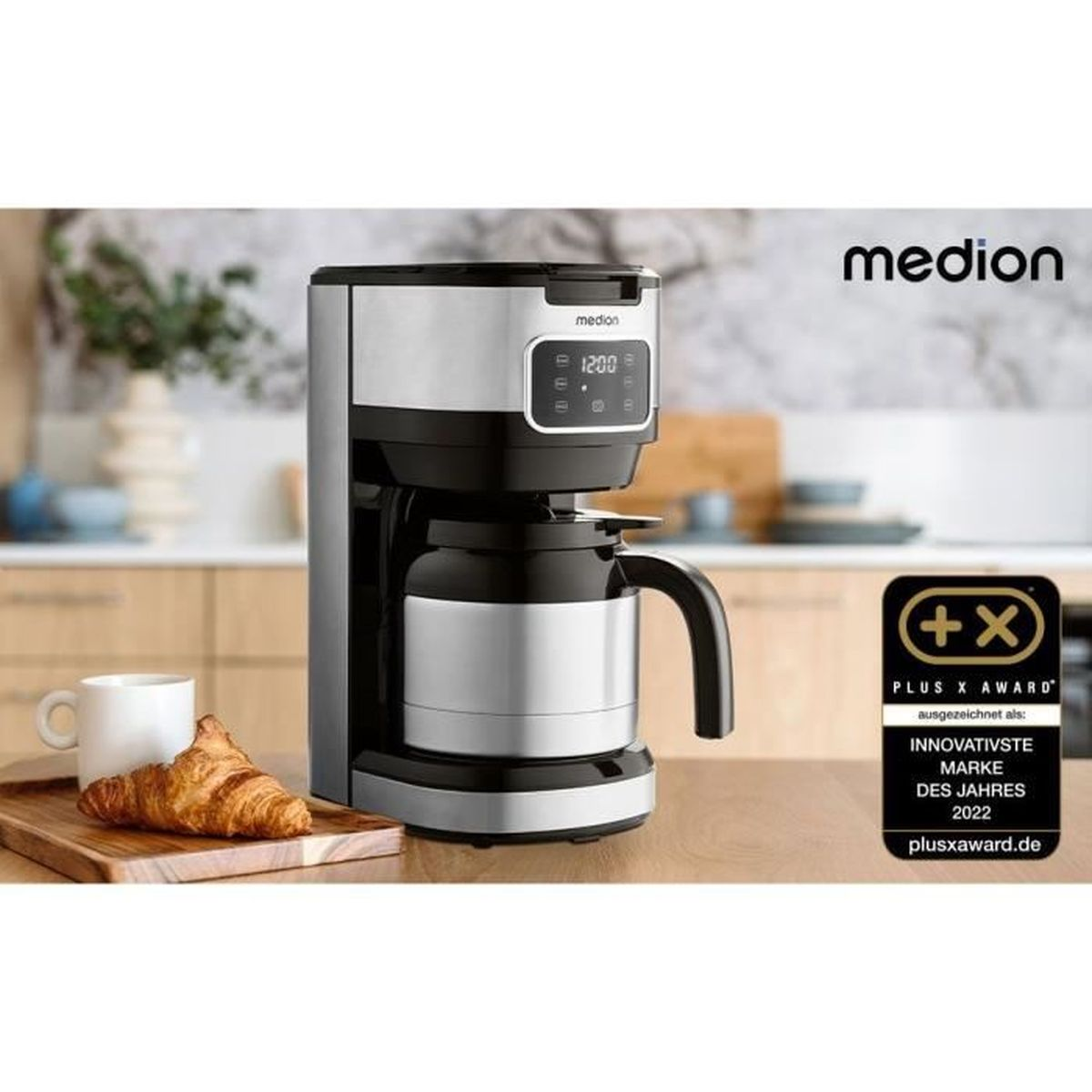 Macchina da caffè Medion argentata con caraffa termica, accanto una tazza e un croissant.