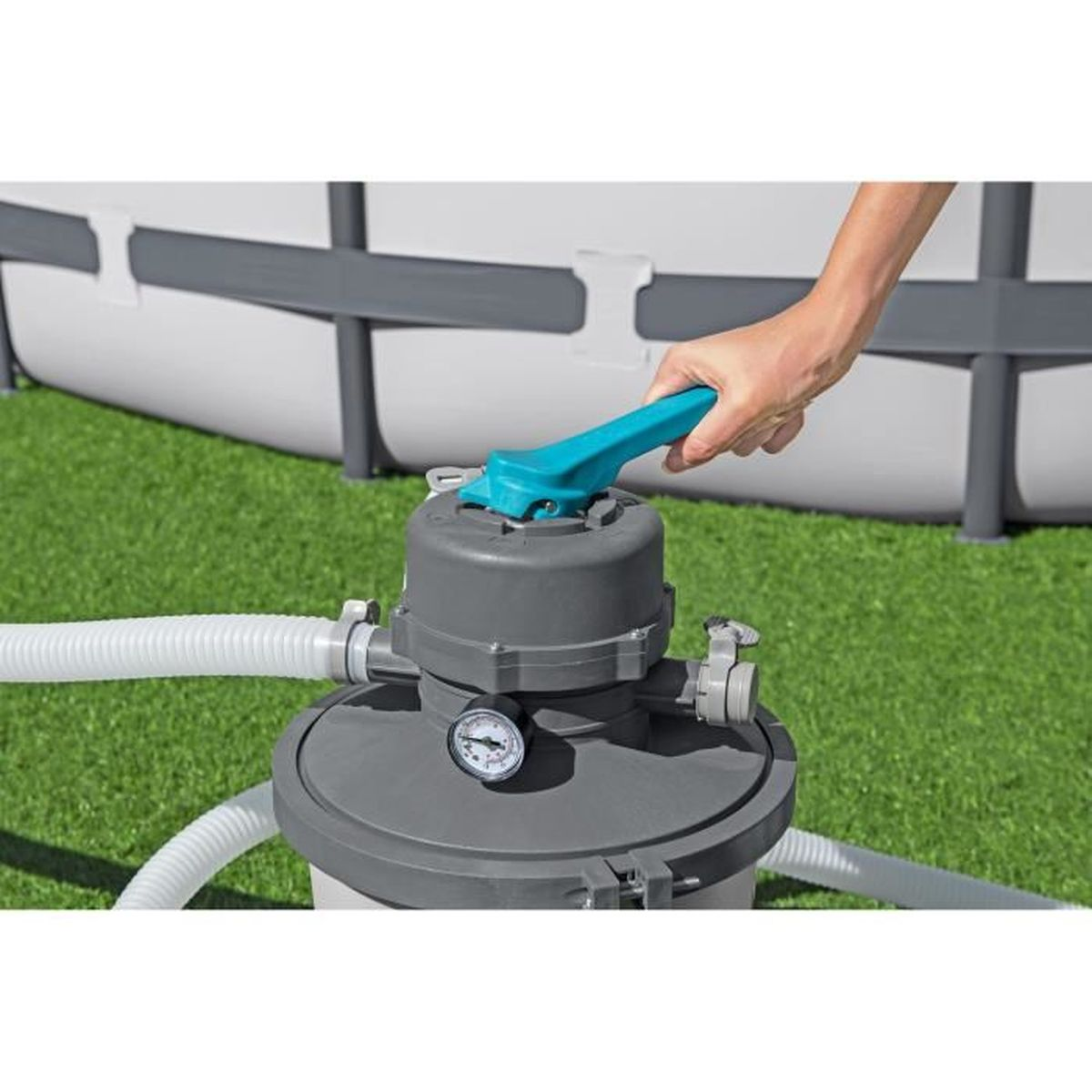 Ręka przekręca niebieską dźwignię na szarym filtrze basenowym z manometrem.