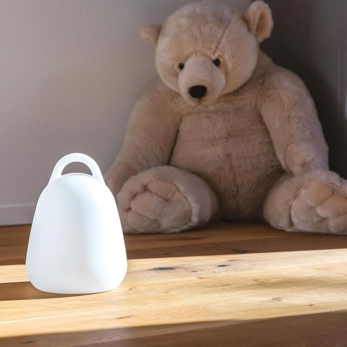 Eine weiße Lampe in Glockenform steht vor einem großen, hellbraunen Teddybären.