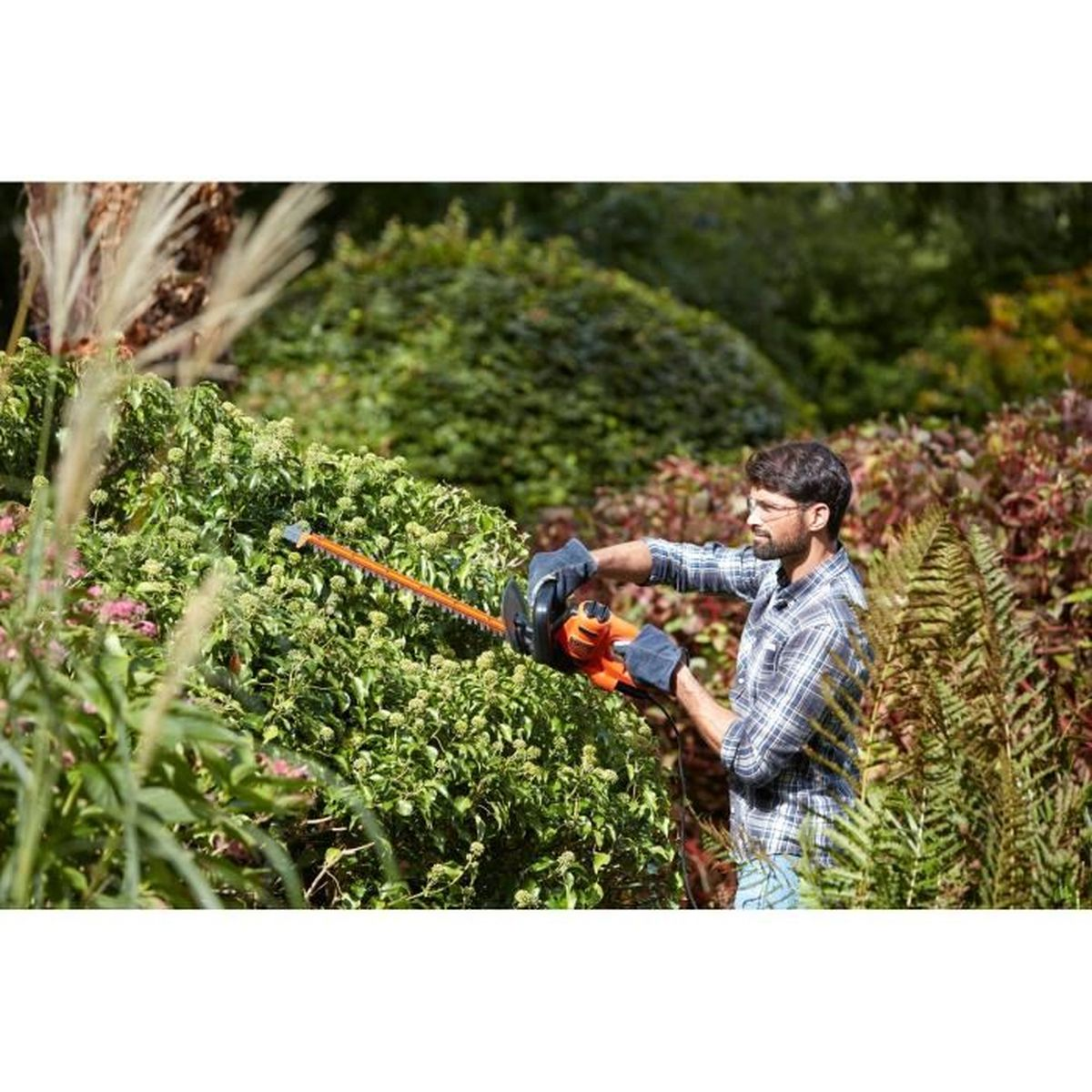 Mężczyzna przycina żywopłot nożycami do żywopłotu w ogrodzie.