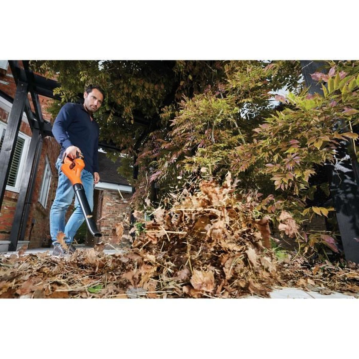 Mężczyzna używa dmuchawy do liści, aby oczyścić suche liście na tarasie.
