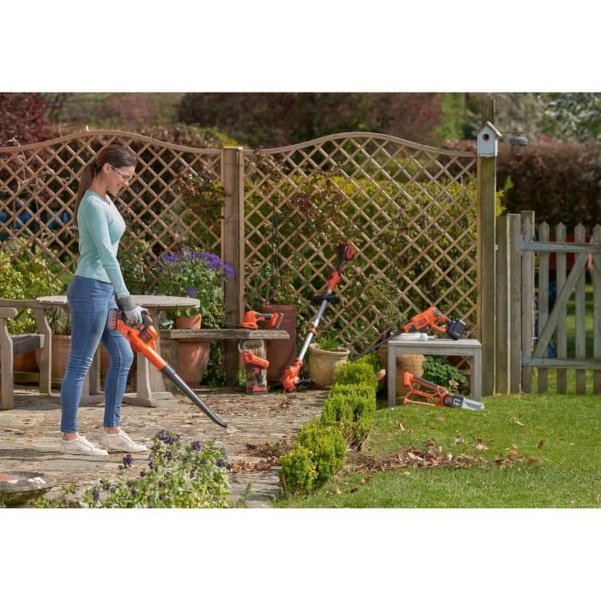 Kobieta dmucha liście dmuchawą w ogrodzie, narzędzia porozrzucane.