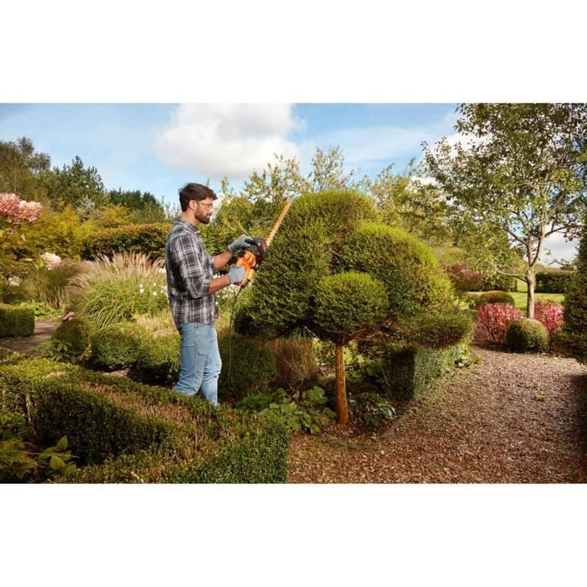 Mężczyzna przycina krzew nożycami do żywopłotu w ogrodzie.