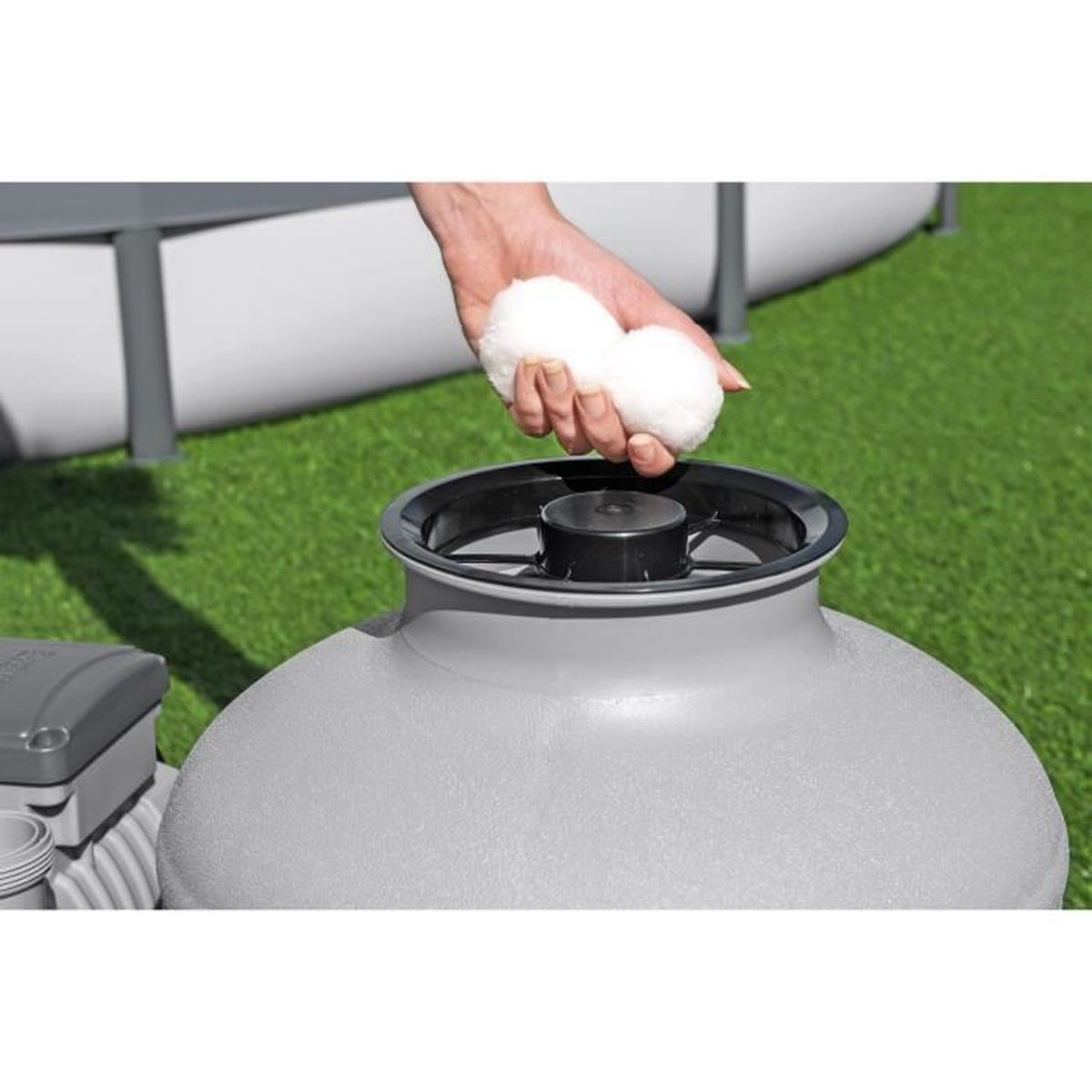 Dłoń trzyma dwie białe kule nad szarym filtrem na trawniku.