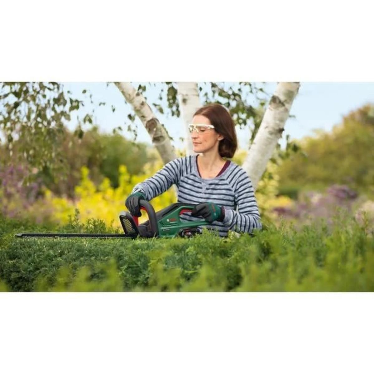 Mujer recorta seto con cortasetos verde, usa gafas y guantes de seguridad.