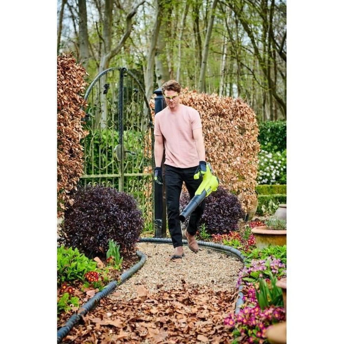 Mann mit Laubbläser geht auf Kiesweg in einem Garten.