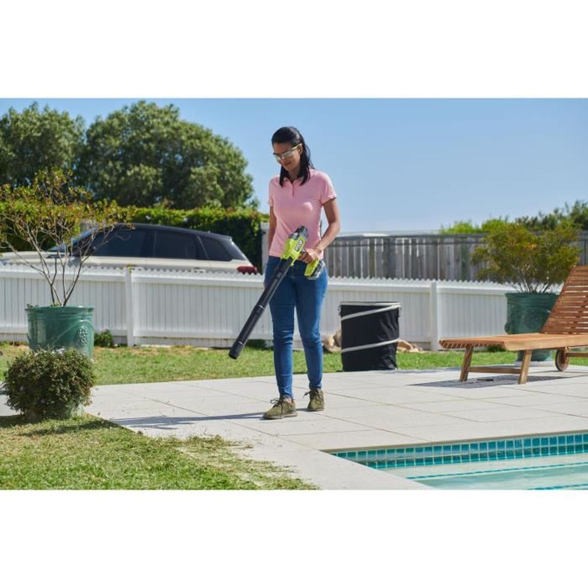 Frau mit Laubbläser im Garten neben Pool und Liegestuhl.