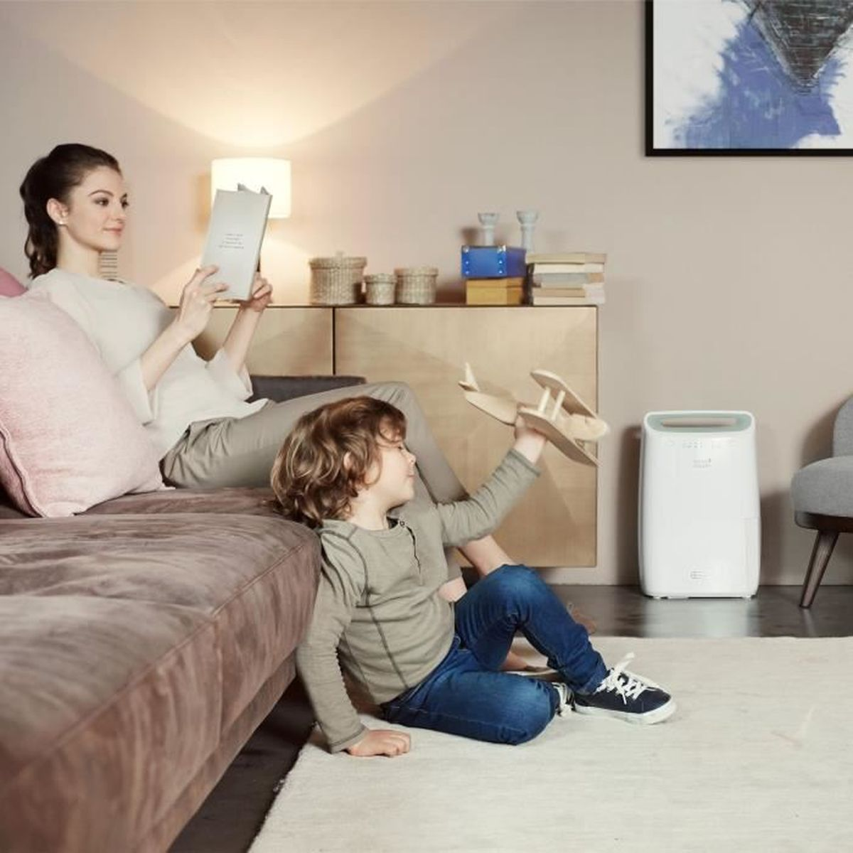 Frau liest Buch, Kind spielt mit Holzflugzeug im Wohnzimmer.