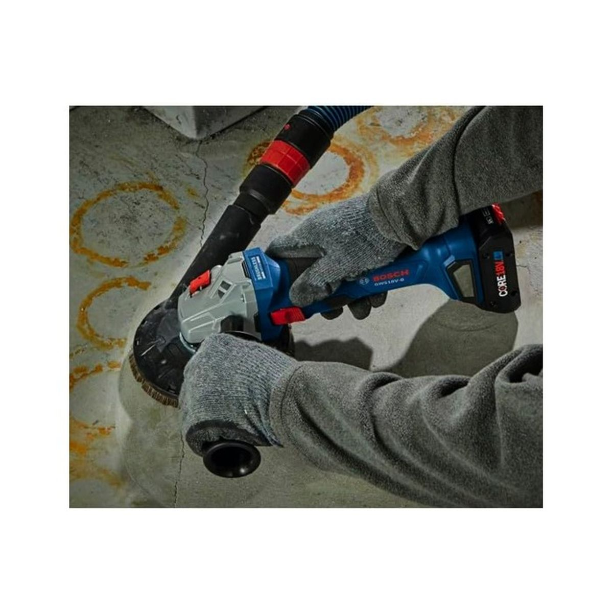 Personne portant des gants utilise une meuleuse d'angle sur un mur en béton avec aspirateur.