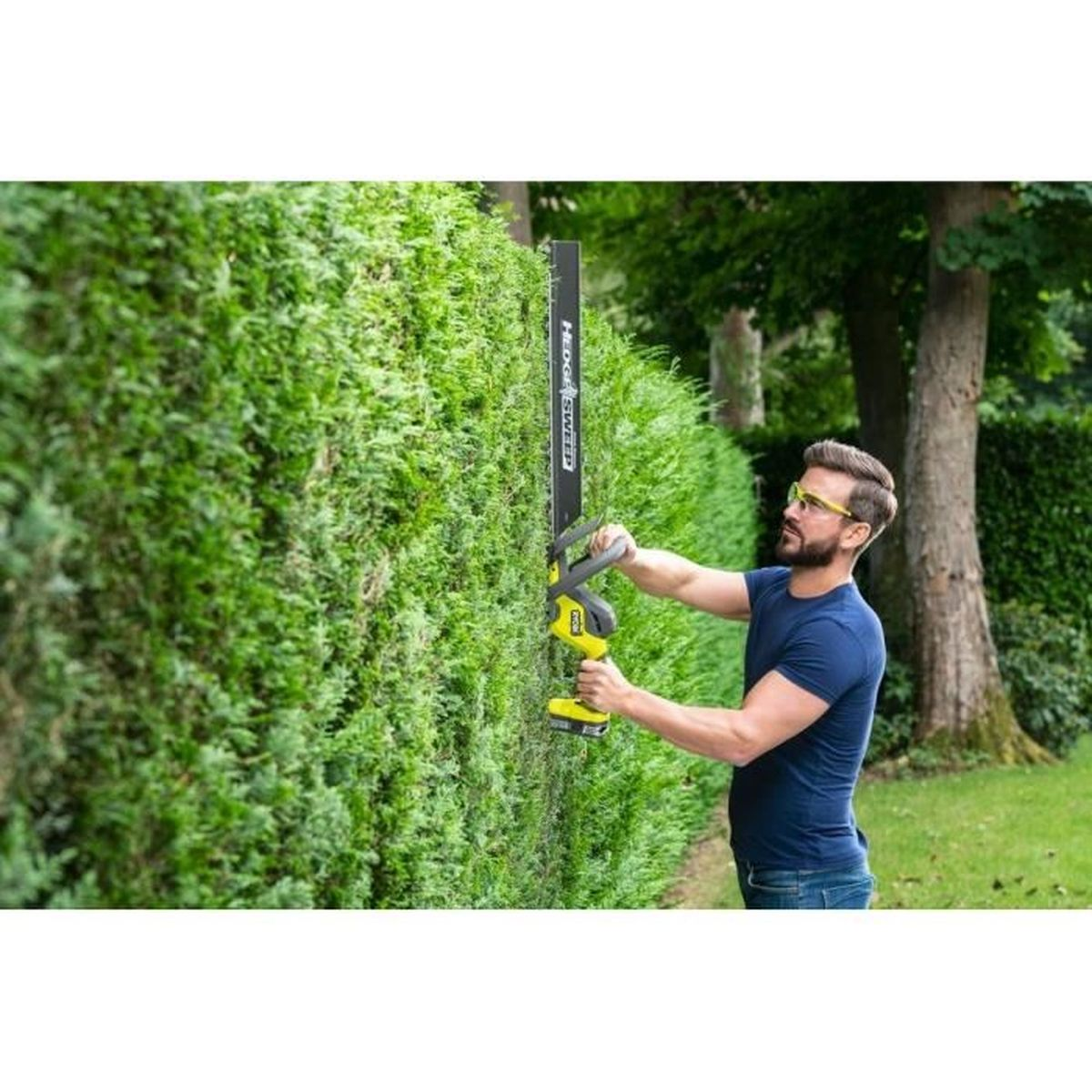 Mann trimmt Hecke mit gelber Heckenschere im Garten.